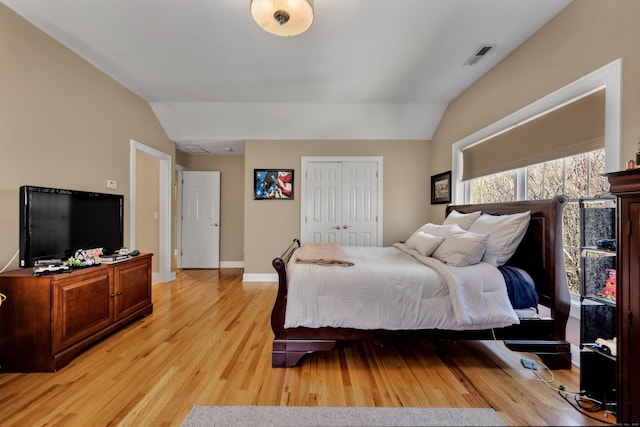 bedroom featuring visible vents, a closet, lofted ceiling, baseboards, and light wood-style flooring