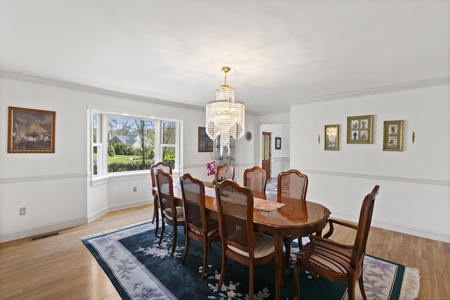 dining room with a chandelier, ornamental molding, light wood finished floors, and visible vents