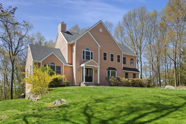 view of front facade with a chimney, a shingled roof, and a front lawn