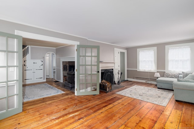 living room with a baseboard heating unit, a fireplace with flush hearth, ornamental molding, and hardwood / wood-style flooring