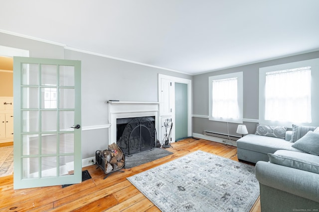 living area featuring a fireplace with raised hearth, a baseboard heating unit, hardwood / wood-style floors, and ornamental molding