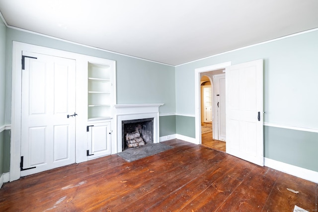 unfurnished living room featuring a fireplace with flush hearth, arched walkways, built in shelves, baseboards, and ornamental molding