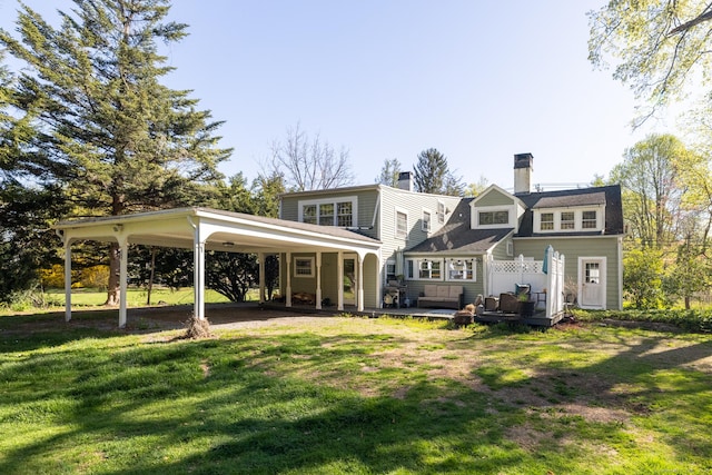 back of property featuring a lawn, a deck, a chimney, and a carport