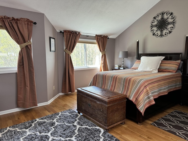 bedroom featuring lofted ceiling, a textured ceiling, baseboards, and wood finished floors