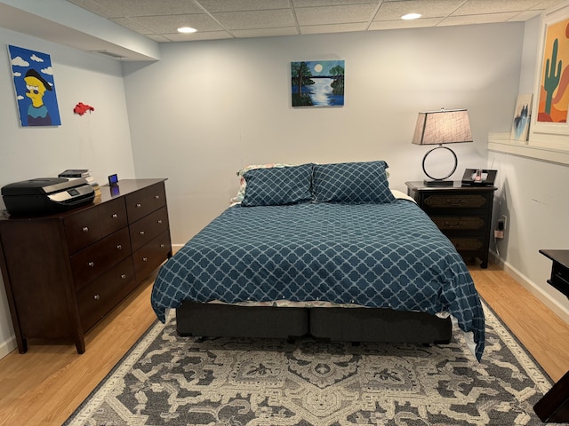 bedroom featuring baseboards, a drop ceiling, and light wood-type flooring
