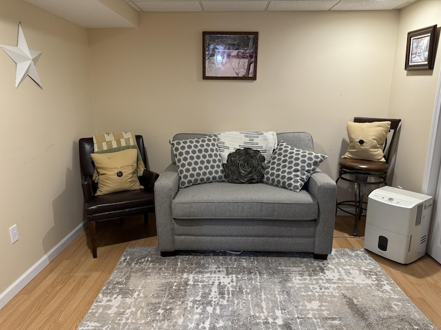 living area featuring a paneled ceiling, baseboards, and wood finished floors