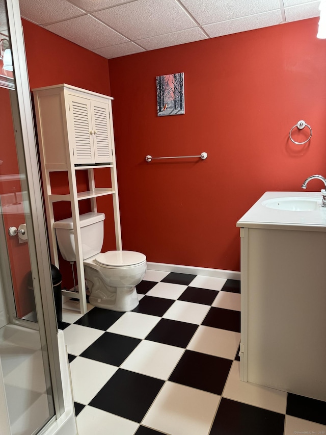 bathroom with toilet, a paneled ceiling, a shower with shower door, tile patterned floors, and vanity