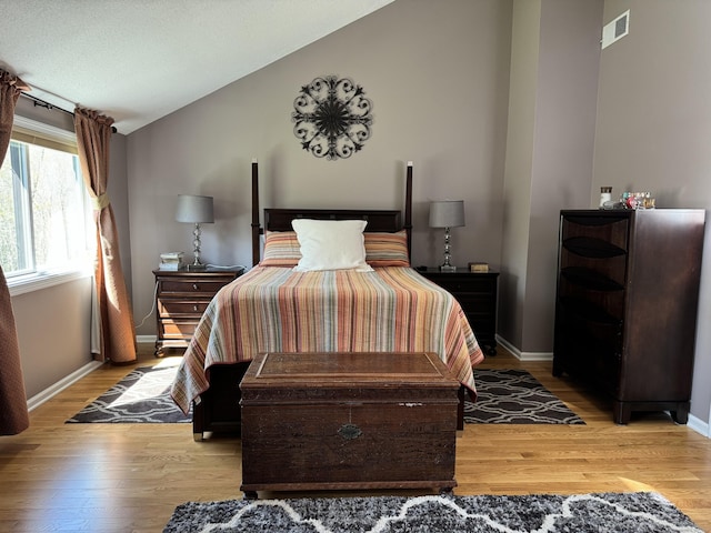 bedroom featuring vaulted ceiling, baseboards, visible vents, and light wood-style floors