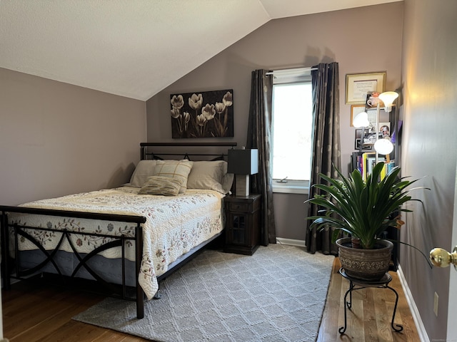 bedroom with vaulted ceiling, wood finished floors, and baseboards