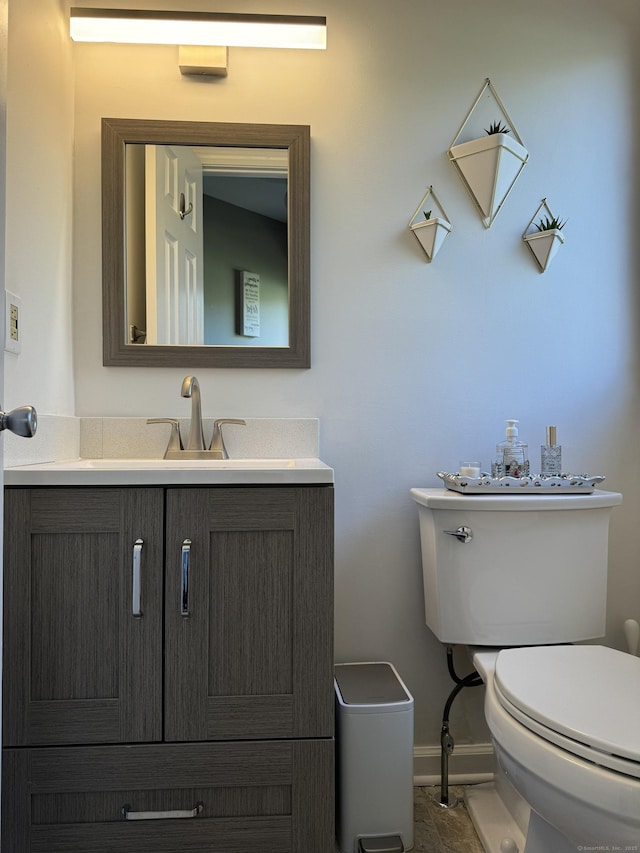 half bathroom with vanity, toilet, and baseboards