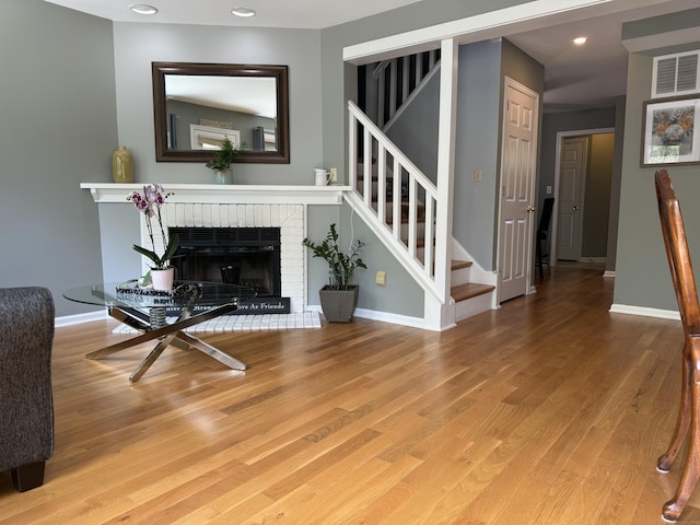 living room with wood finished floors, a brick fireplace, visible vents, baseboards, and recessed lighting