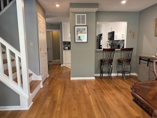 kitchen featuring fridge, visible vents, a kitchen bar, black microwave, and white cabinets