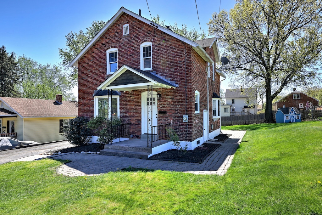 traditional home with fence, a front yard, brick siding, a storage unit, and an outbuilding