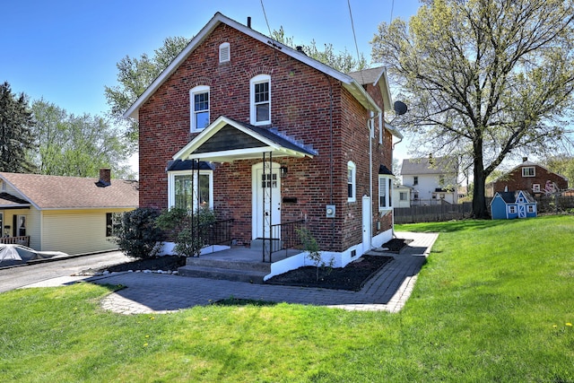 traditional home with fence, a front yard, brick siding, a storage unit, and an outbuilding