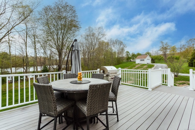 wooden terrace featuring a water view, outdoor dining space, a yard, area for grilling, and an outbuilding