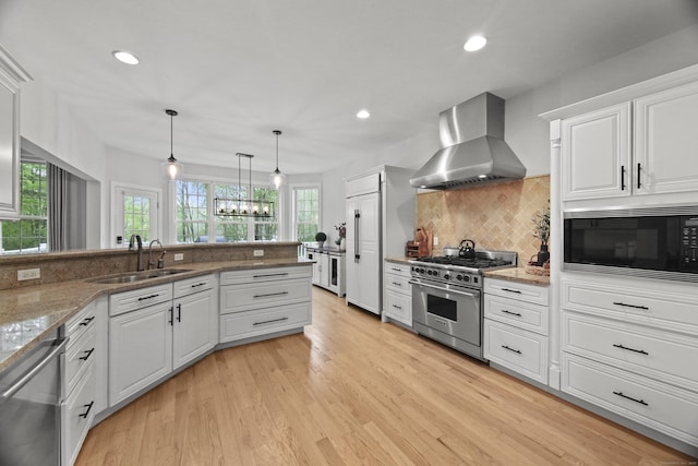 kitchen with a sink, stainless steel appliances, wall chimney range hood, recessed lighting, and white cabinetry