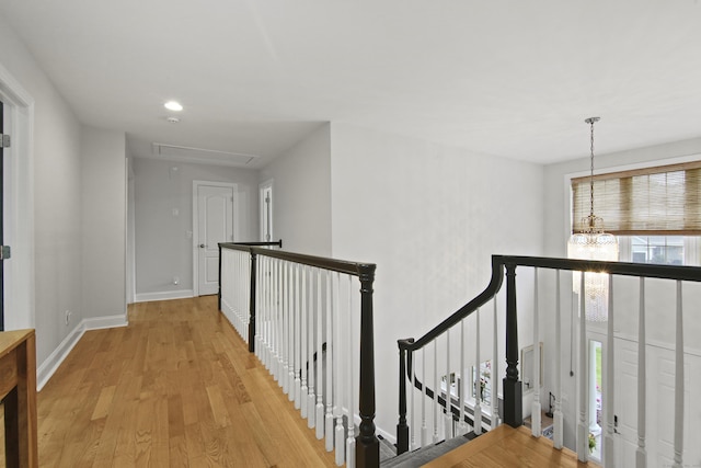 corridor with attic access, baseboards, an upstairs landing, a notable chandelier, and light wood-style floors