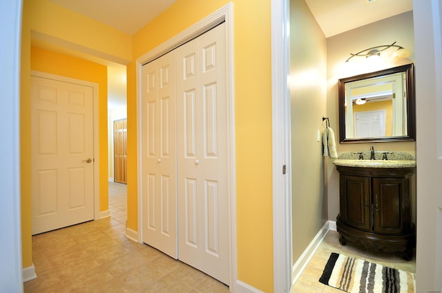 corridor featuring baseboards, light tile patterned floors, and a sink