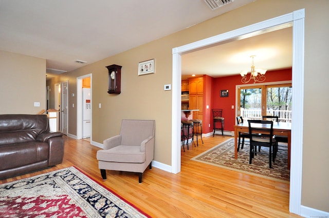 living area with visible vents, light wood-style flooring, a chandelier, and baseboards