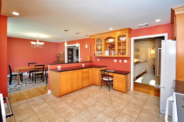 kitchen featuring glass insert cabinets, dark countertops, visible vents, freestanding refrigerator, and a peninsula