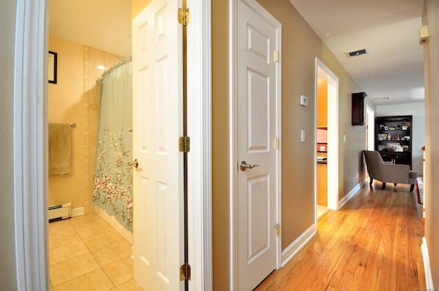 hall featuring visible vents, light wood finished floors, baseboard heating, and baseboards