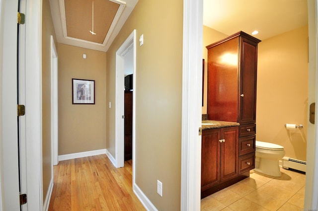 corridor with attic access, light wood-style flooring, a baseboard heating unit, and baseboards