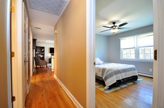 hallway featuring baseboards, visible vents, wood finished floors, and a baseboard radiator