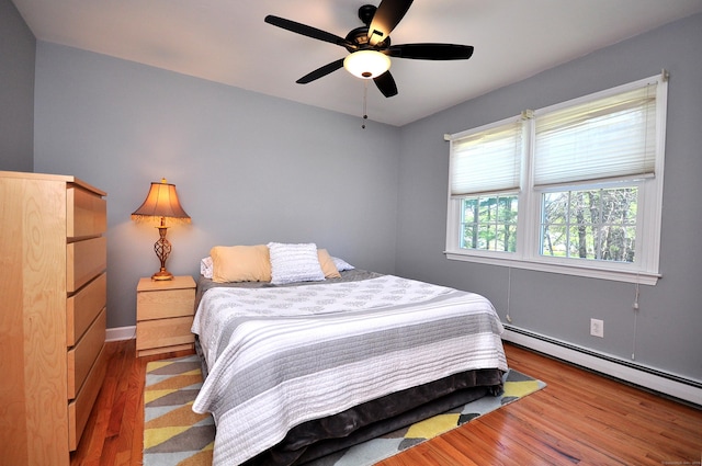 bedroom with wood finished floors, ceiling fan, and baseboard heating