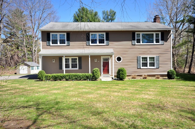 traditional-style house featuring an outdoor structure, a front lawn, covered porch, and a chimney