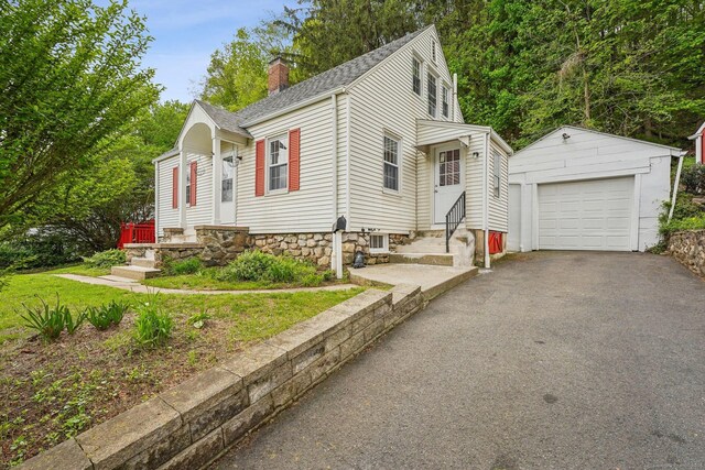 view of front of property with an outbuilding, a chimney, entry steps, a detached garage, and asphalt driveway