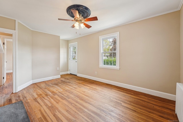 spare room with baseboards, light wood-style floors, ceiling fan, radiator heating unit, and ornamental molding