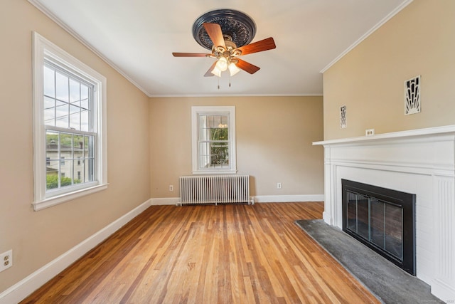 unfurnished living room with radiator heating unit, a glass covered fireplace, wood finished floors, baseboards, and ornamental molding