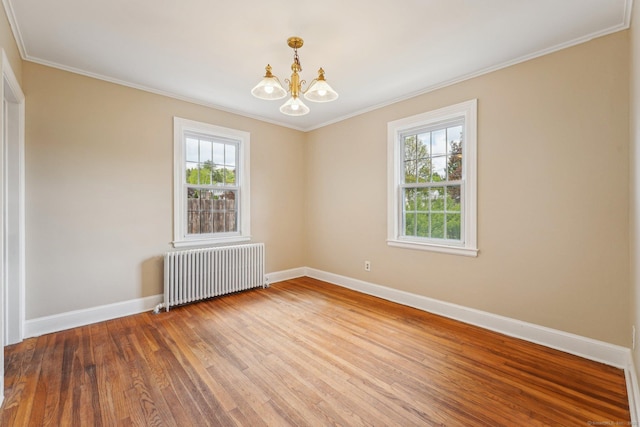 spare room with radiator, baseboards, a chandelier, wood finished floors, and crown molding