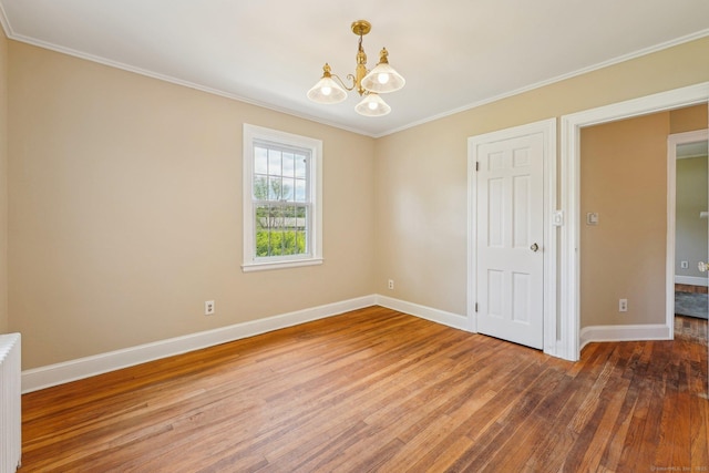 empty room featuring a chandelier, wood-type flooring, baseboards, and ornamental molding