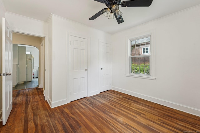 unfurnished bedroom featuring dark wood finished floors, baseboards, arched walkways, a closet, and crown molding