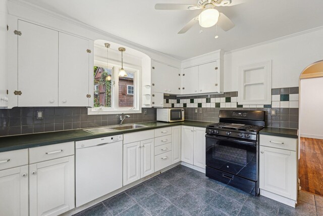 kitchen featuring gas stove, white dishwasher, dark countertops, a sink, and crown molding