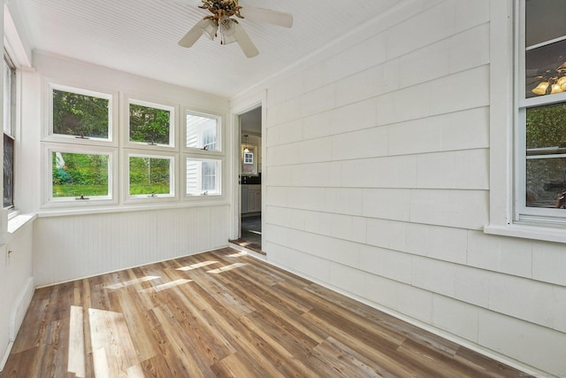 unfurnished room with wood finished floors, a ceiling fan, and wood walls
