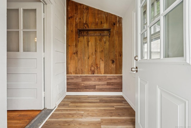 entryway with wood finished floors, vaulted ceiling, wood walls, and baseboards