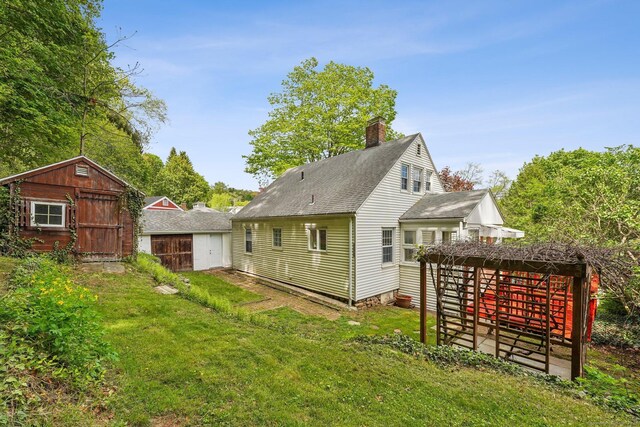 back of property with a shed, a chimney, an outbuilding, a lawn, and a shingled roof