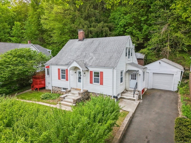 cape cod-style house with an outdoor structure, a chimney, asphalt driveway, roof with shingles, and a garage