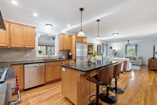 kitchen with a sink, light wood-style floors, a kitchen breakfast bar, appliances with stainless steel finishes, and open floor plan