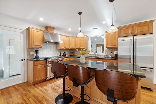 kitchen featuring a breakfast bar area, light wood-style floors, wall chimney exhaust hood, high end appliances, and backsplash