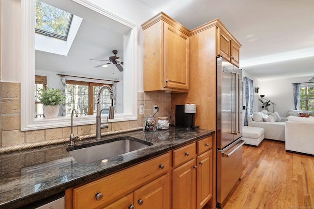 kitchen with dark stone counters, a sink, light wood-style floors, high quality fridge, and a skylight