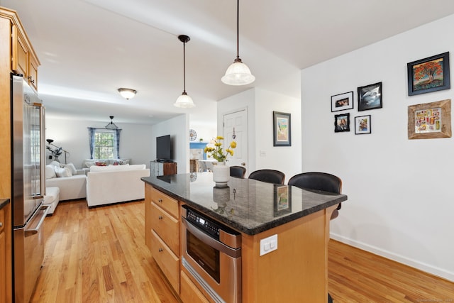 kitchen featuring stainless steel appliances, a center island, a breakfast bar area, light wood-style flooring, and pendant lighting