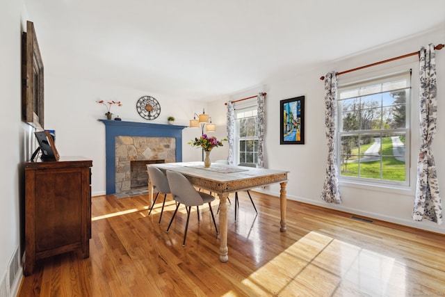 dining space featuring visible vents, light wood finished floors, a stone fireplace, and baseboards