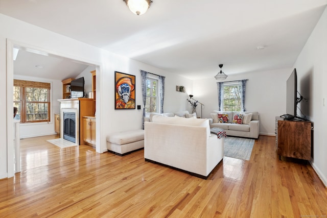 living room featuring baseboards, a fireplace with flush hearth, and light wood-style floors