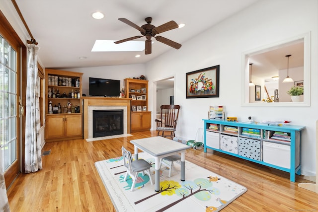 living area featuring a fireplace with flush hearth, wood finished floors, a ceiling fan, and lofted ceiling with skylight