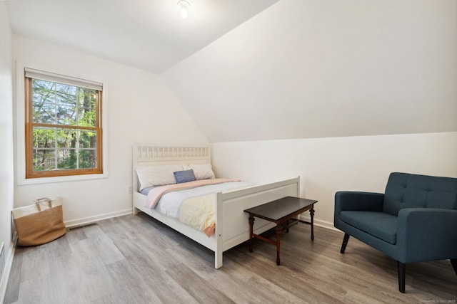 bedroom with light wood finished floors, visible vents, vaulted ceiling, and baseboards