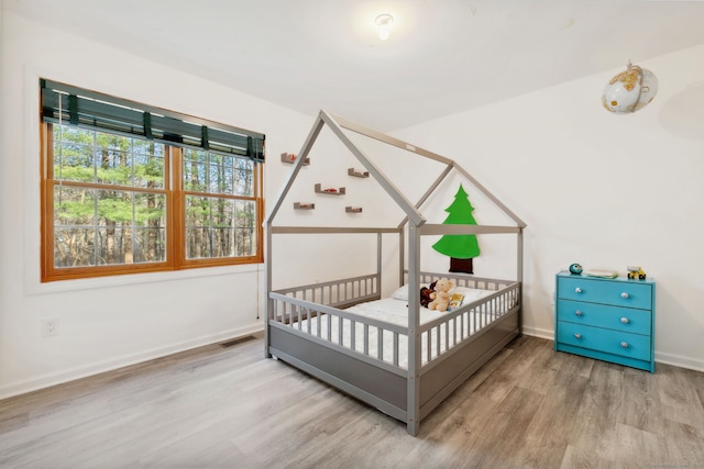 bedroom featuring wood finished floors, a crib, visible vents, and baseboards