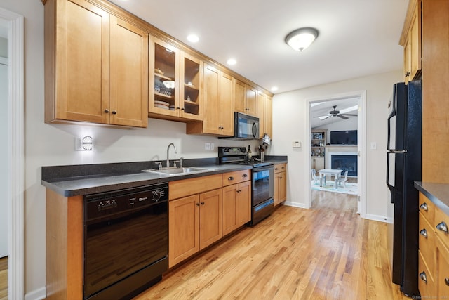 kitchen featuring a sink, a fireplace, black appliances, a ceiling fan, and dark countertops
